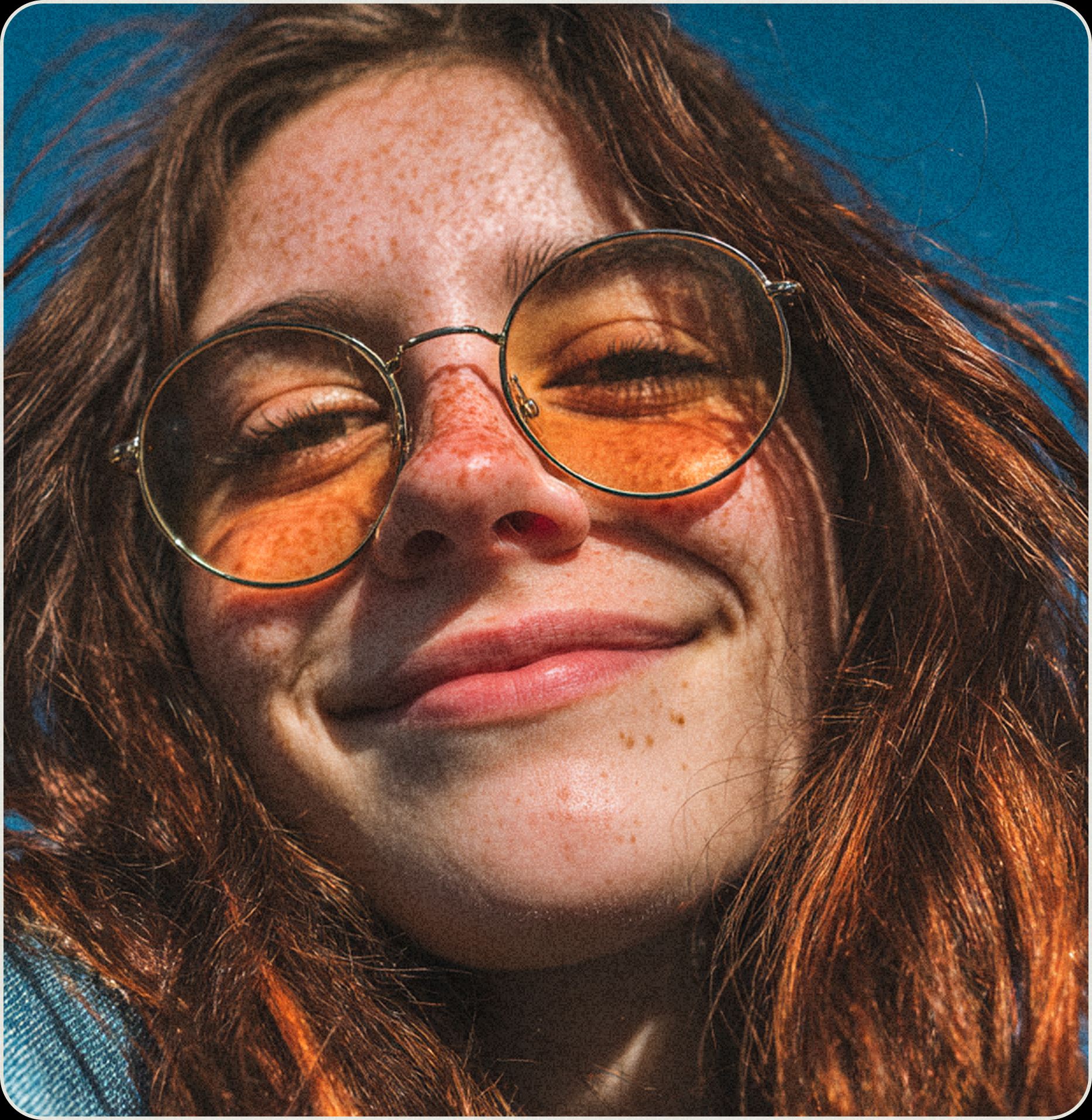 Smiling person with freckles and round orange-tinted glasses